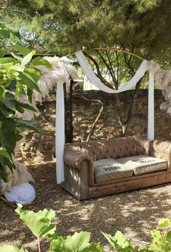 Sofá de estilo vintage rodeado de plantas y decorado con telas blancas.