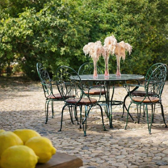Mesa de hierro forjado con sillas, decorada con flores, en un entorno natural. Limones al frente.