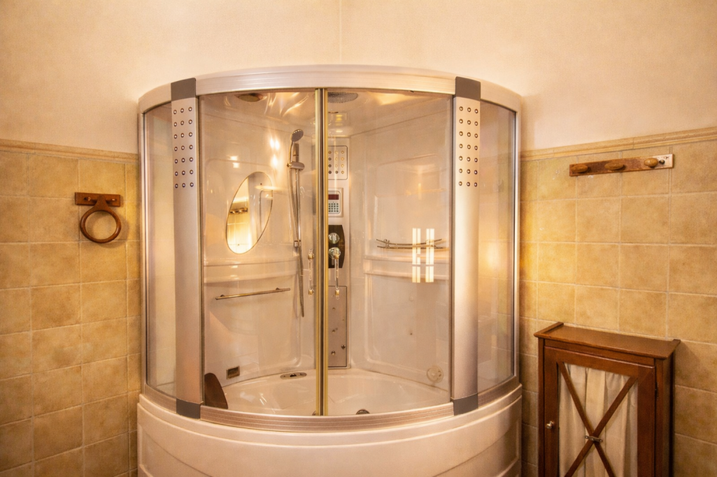 Ducha circular de vidrio en un baño, con luces y pared de azulejos claros.