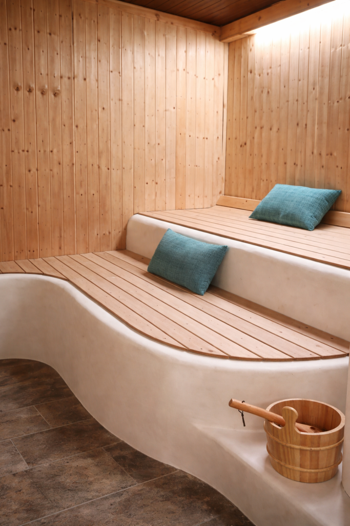 Interior de sauna con bancos de madera y cojines azules, y un cubo de madera.