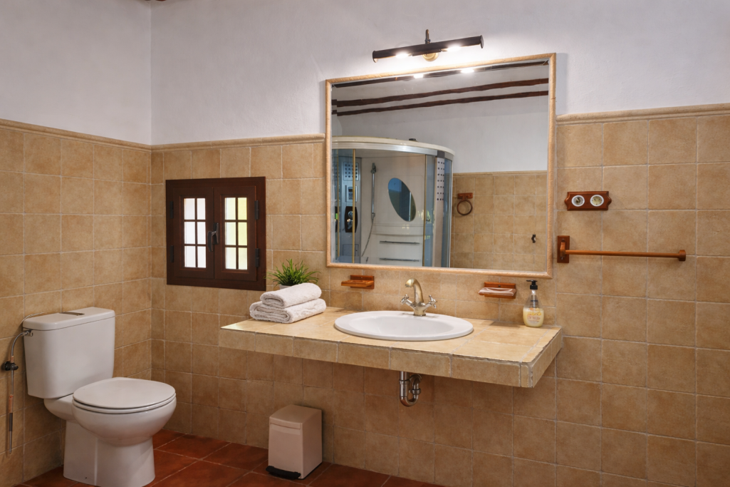 Baño moderno con lavabo, espejo grande, inodoro y toallas sobre la encimera.