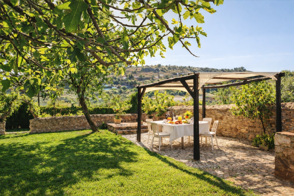 Mesa con sillas bajo pérgola en un jardín con vistas a la naturaleza.